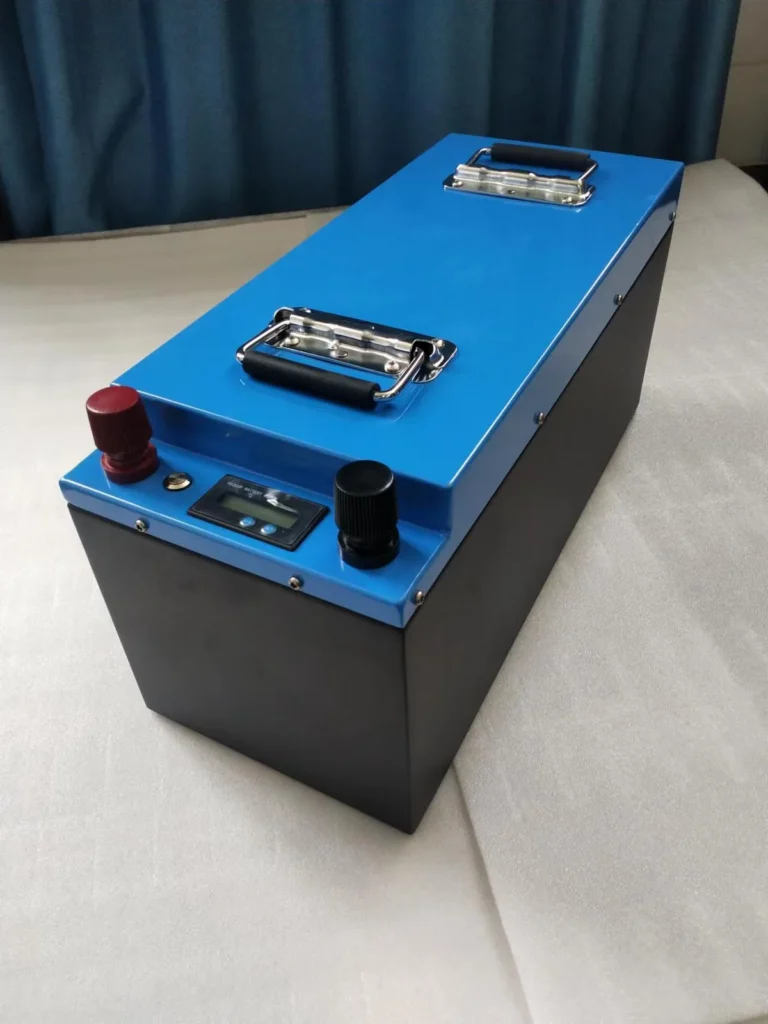 Blue and black metal-case LiFePO4 battery with two carry handles, red and black terminal knobs and a small digital battery meter on the end panel